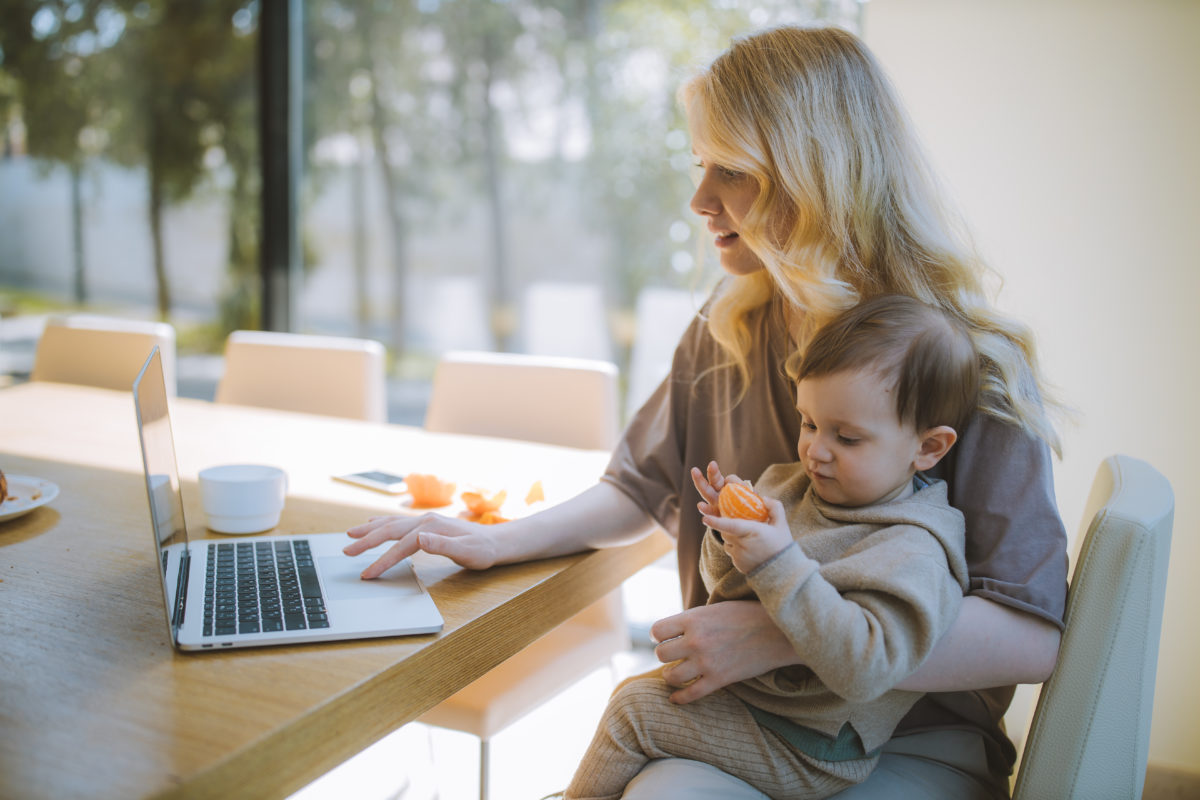 Woman carrying her baby and working on a laptop